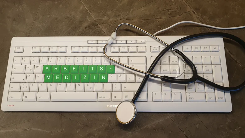Stethoskop auf Computertastatur, Aufschrift »Arbeitsmedizin« auf Tastatur
