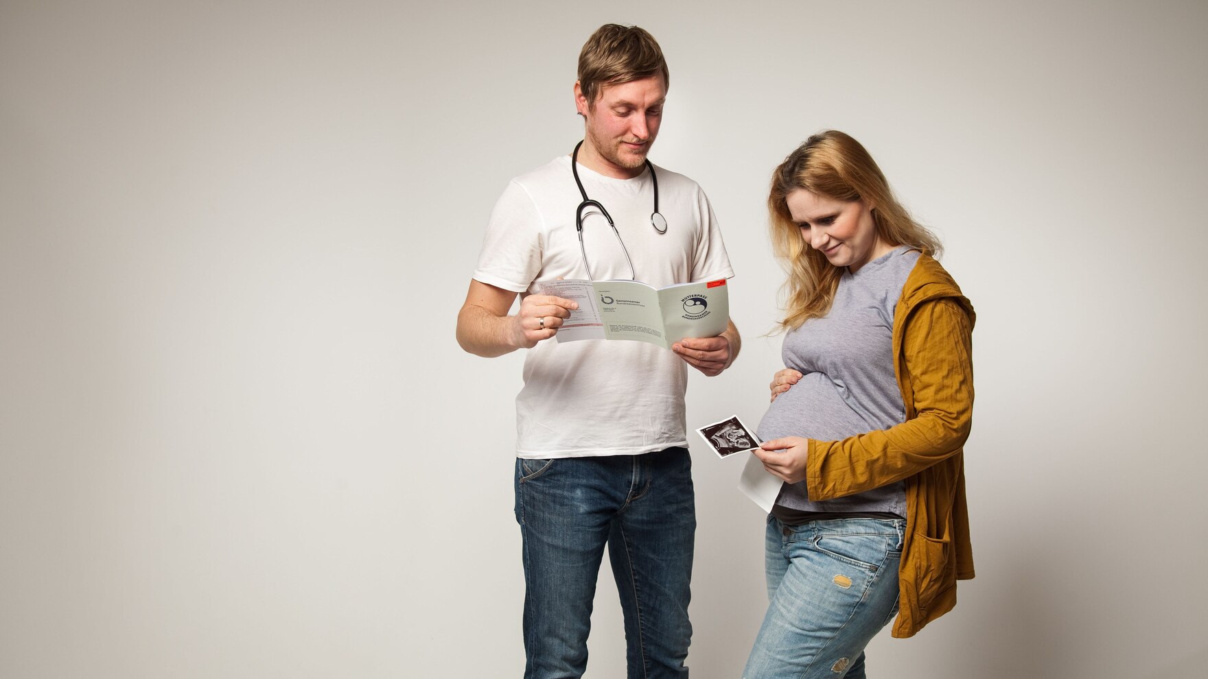 Schwangere hält lächelnd ihr Ultraschallbild in der Hand während der Arzt den Mutterpass ansieht