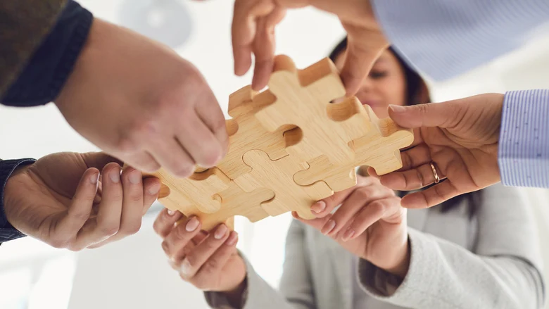 Menschen fügen verschiedene Puzzleteile aus Holz zusammen