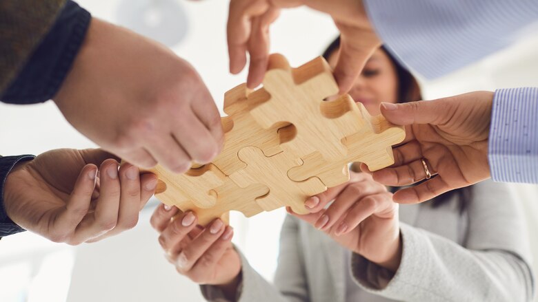 Menschen fügen verschiedene Puzzleteile aus Holz zusammen